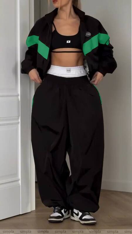 Person wearing a black and green jacket with high-waisted pants indoors.