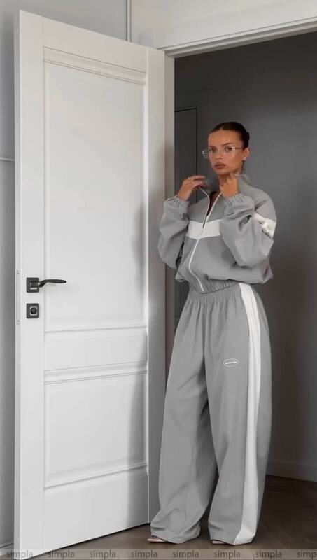 Person wearing a gray tracksuit standing in a room with a white door.