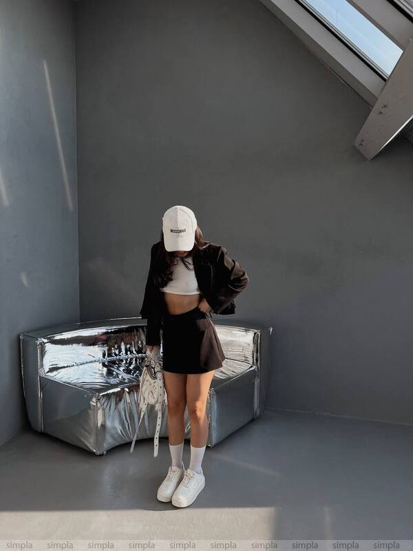 Person wearing a white cap and dark jacket in a minimalistic room with a reflective surface.
