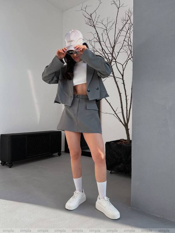Person wearing a gray outfit with a white top and white sneakers, standing in a minimalistic room.