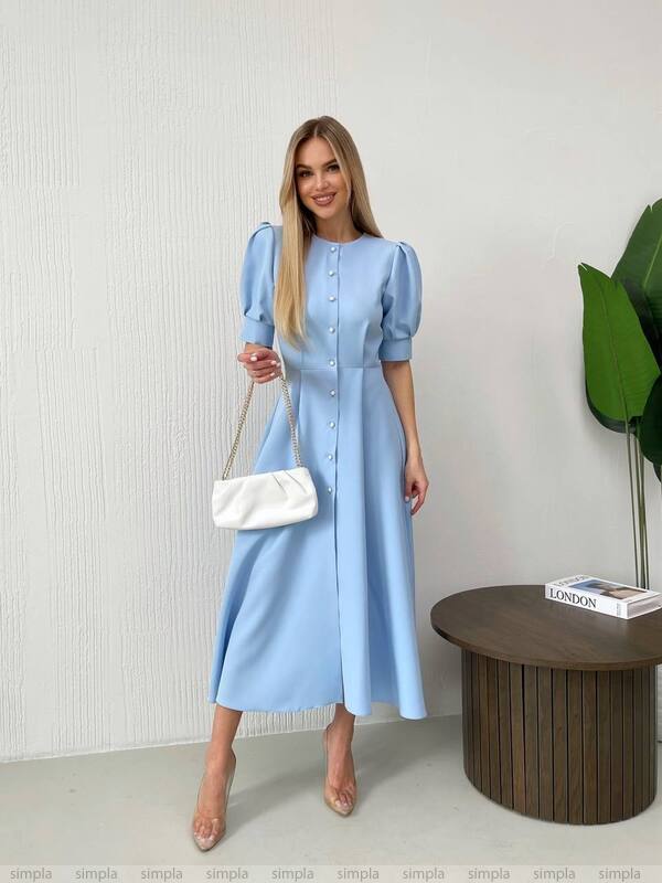 Woman in a light blue dress holding a white bag against a neutral background