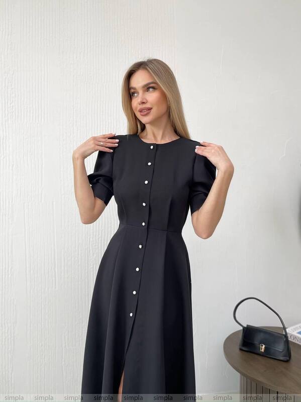 Woman wearing a black dress with white buttons against a plain background