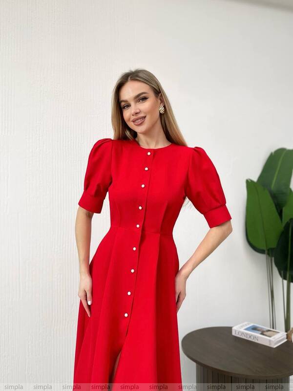 Woman wearing a red dress with puff sleeves against a white wall.