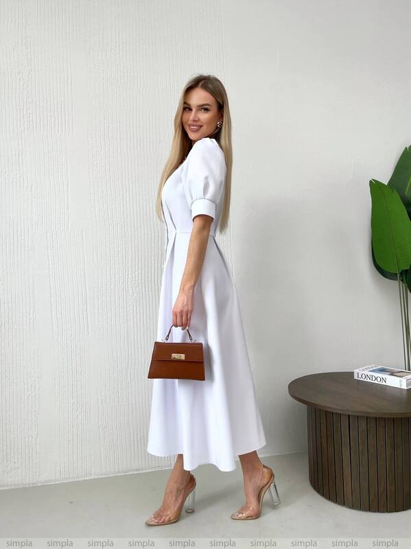Woman in a white dress holding a brown handbag against a plain background