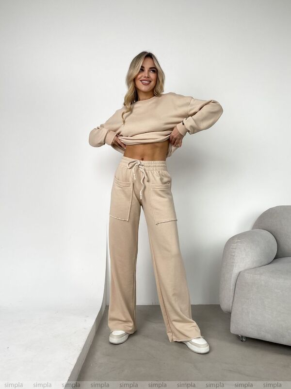 Woman wearing a beige outfit standing in a minimalistic room with a gray sofa.