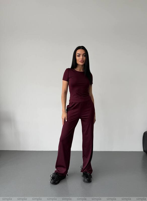 Woman wearing a maroon jumpsuit against a plain background