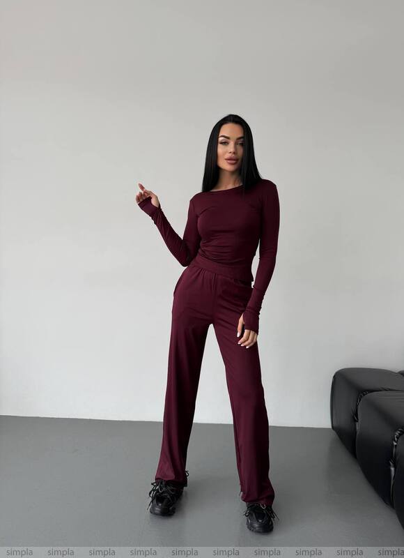 Woman wearing a burgundy jumpsuit against a plain background