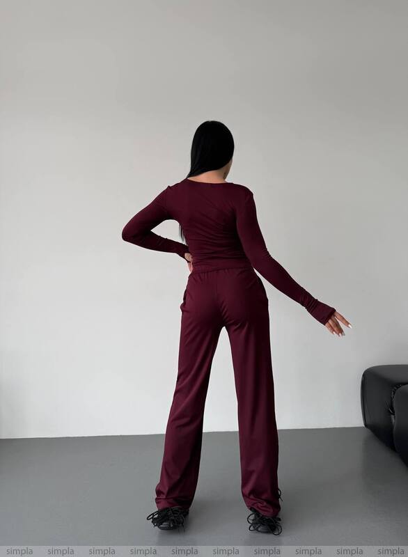 Person wearing a burgundy outfit standing against a plain background
