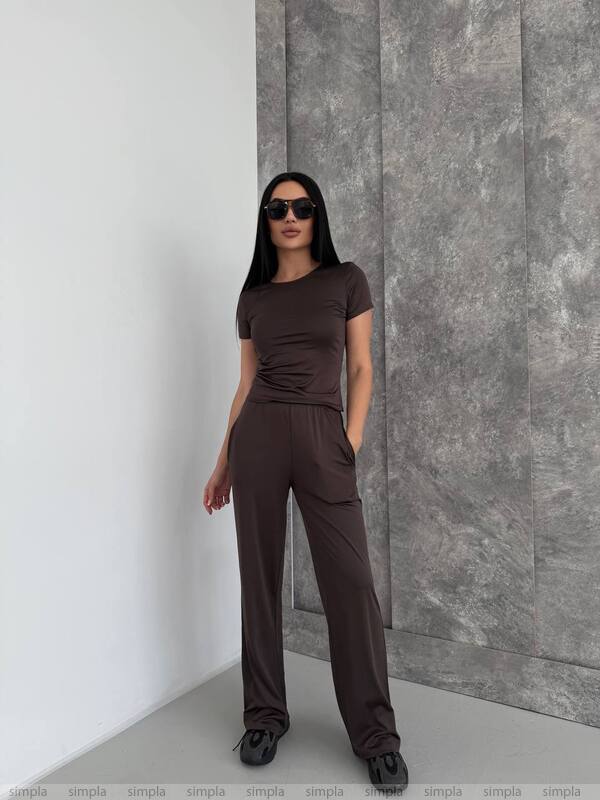 Woman wearing a brown outfit standing against a gray wall.