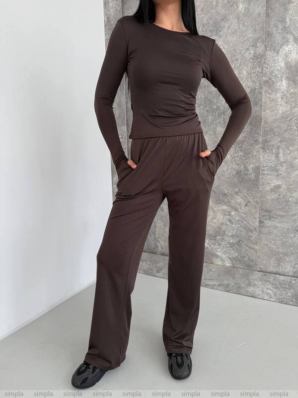 Person wearing a brown outfit against a gray wall.