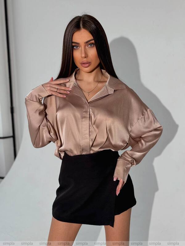 Woman wearing a beige satin blouse and black skirt against a plain background