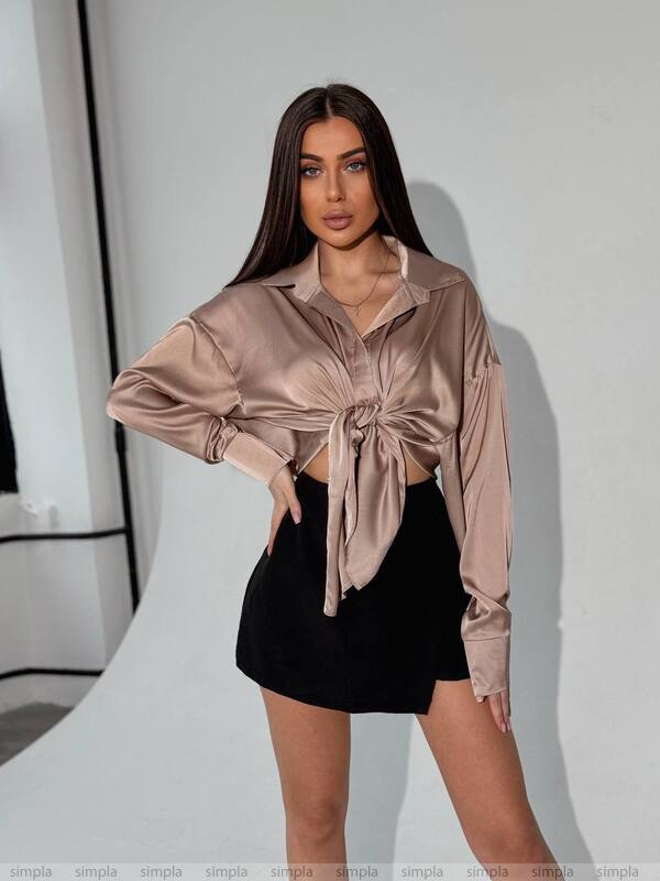 Woman wearing a beige satin shirt and black shorts against a white background