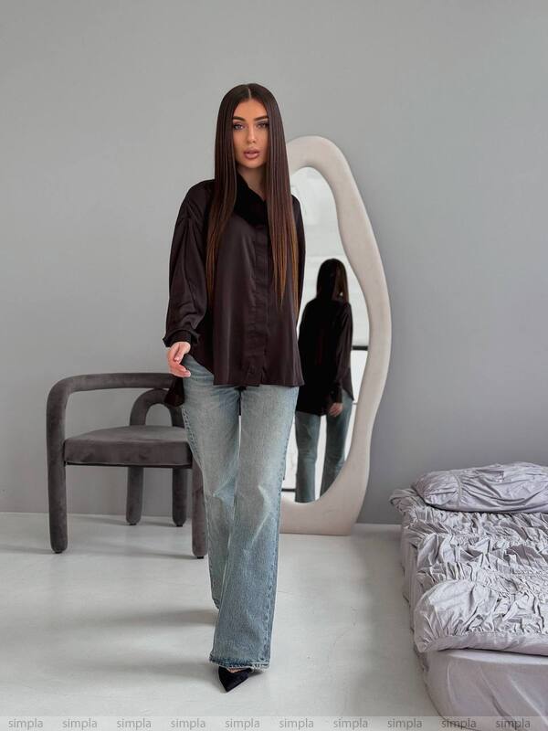 Woman standing in a room with a large mirror and gray walls.