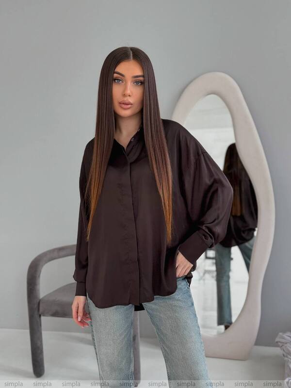 Woman wearing a dark brown oversized shirt and light blue jeans standing in front of a mirror.