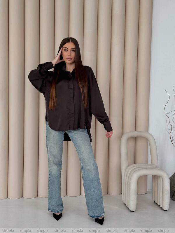 Woman wearing a black blouse and light blue jeans standing against a beige curtain.