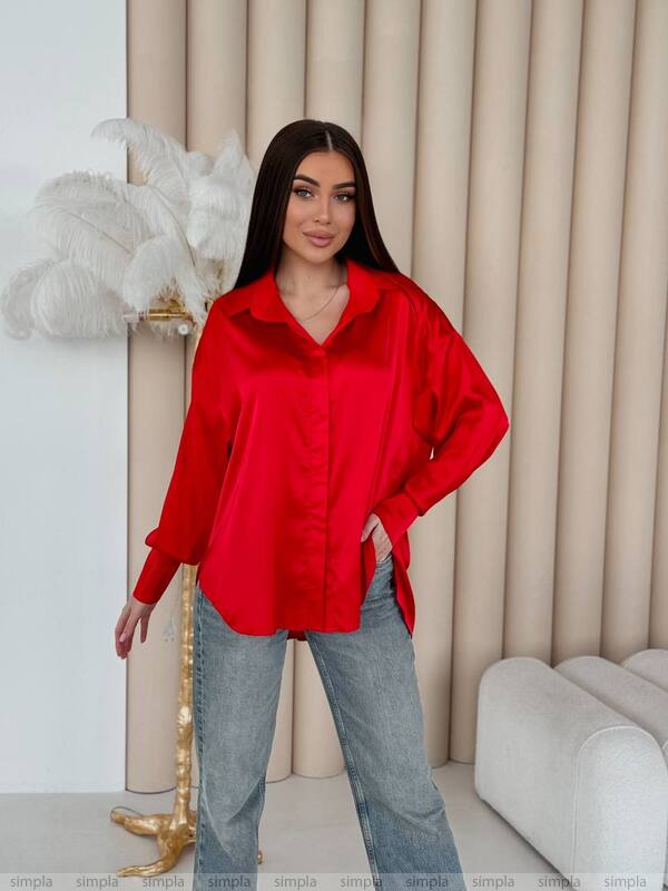 Woman wearing a red shirt and blue jeans standing in a room with decorative elements.
