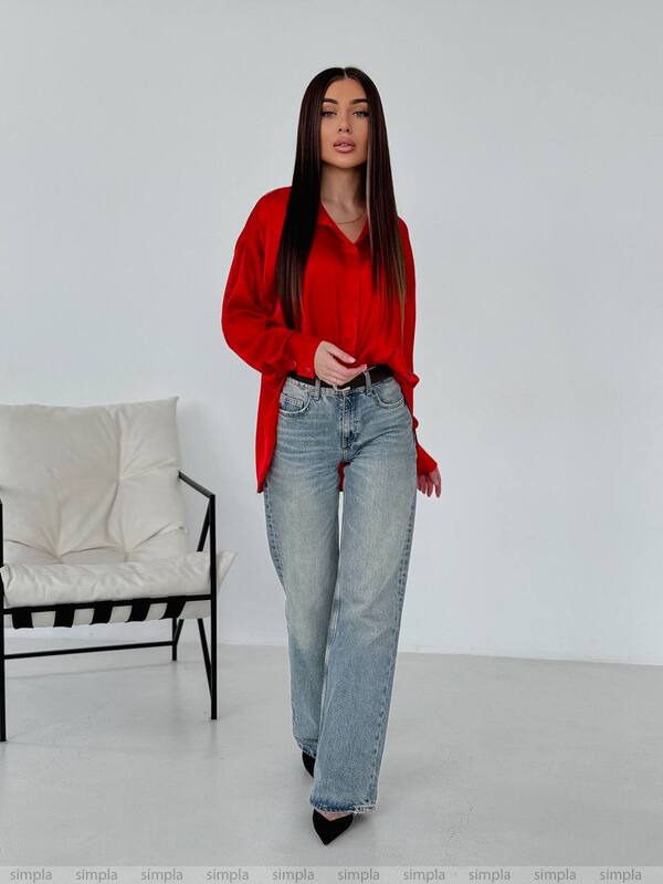 Woman wearing a red blouse and blue jeans standing in a minimalistic room.