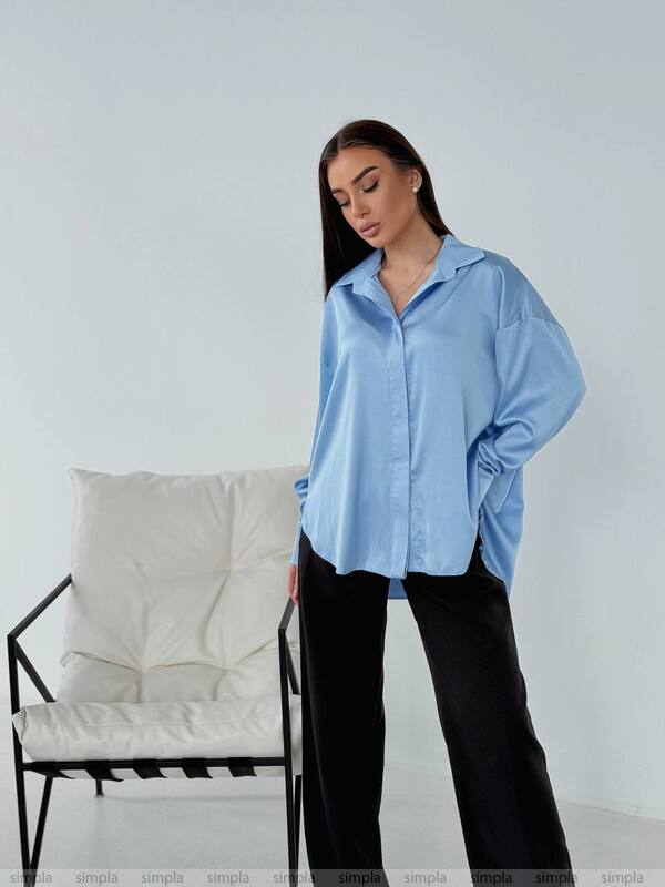 Woman wearing a light blue shirt and black pants in a minimalistic room.