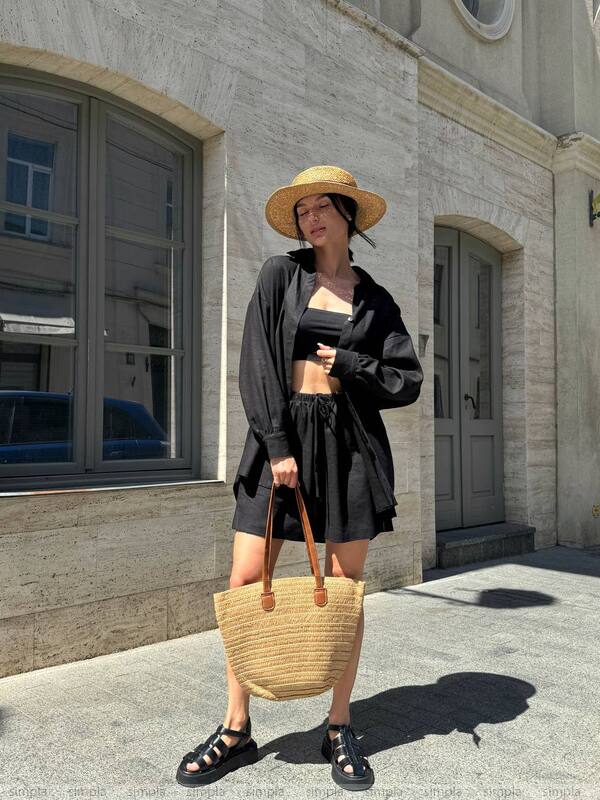 Woman in black outfit with straw hat and bag standing in front of a building
