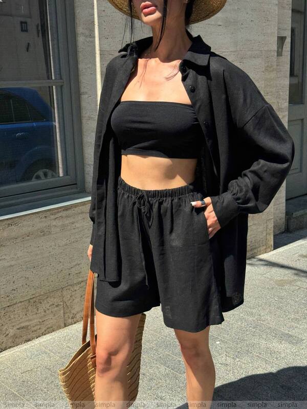 Person wearing a black outfit with a straw hat and bag, standing outdoors.