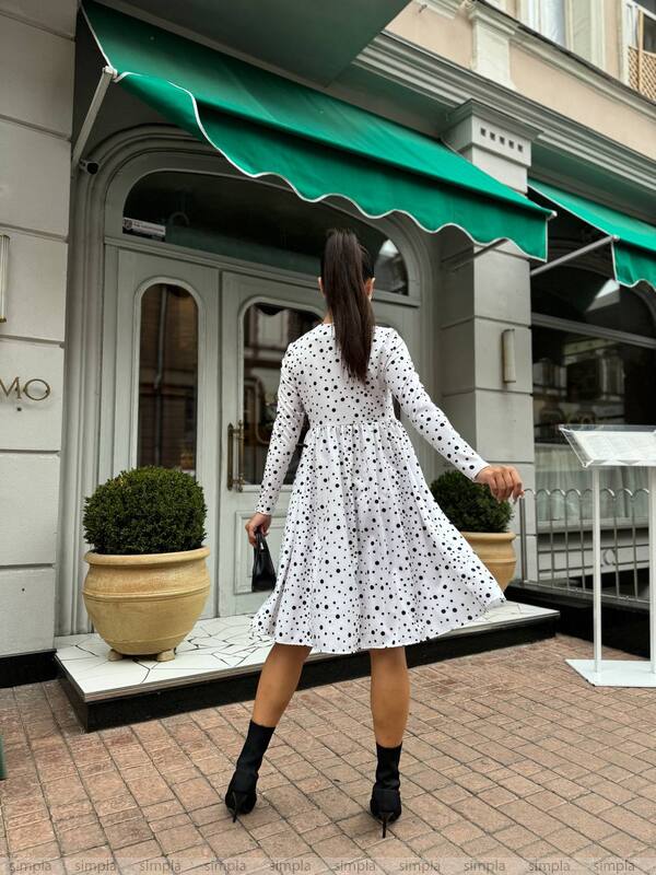 Woman in a polka dot dress walking past a building with a green awning.