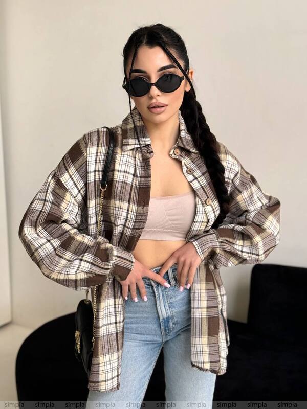 Woman wearing a plaid shirt over a crop top and jeans, with sunglasses on.