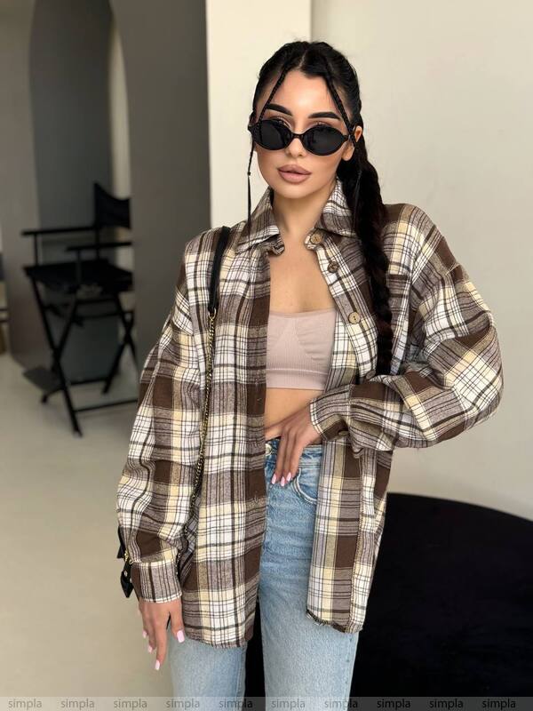 Person wearing a plaid shirt, beige top, and jeans indoors.