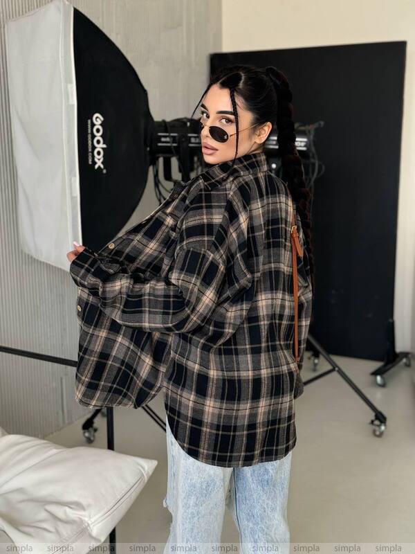 Person wearing a plaid shirt in a photography studio setting with lighting equipment.