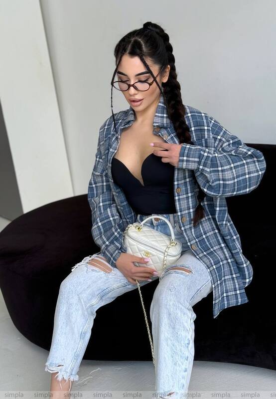 Woman wearing a blue plaid shirt, black top, and light blue jeans, sitting on a black chair.