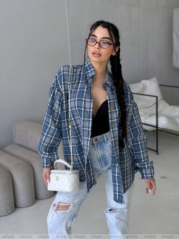 Woman wearing a blue plaid shirt and ripped jeans in a living room setting.
