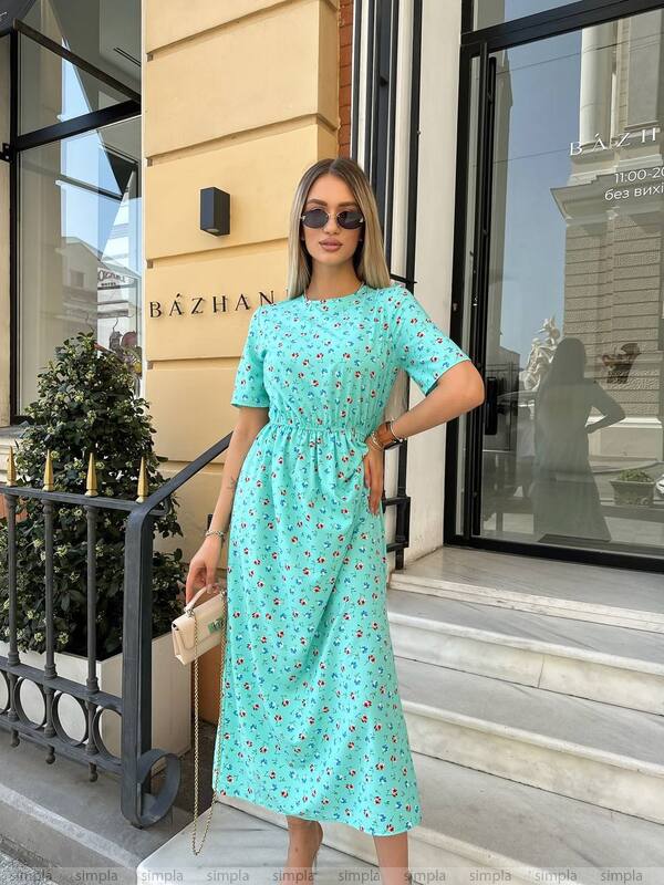 Woman in a turquoise dress standing outside a building with 'Bázhan' on the wall.