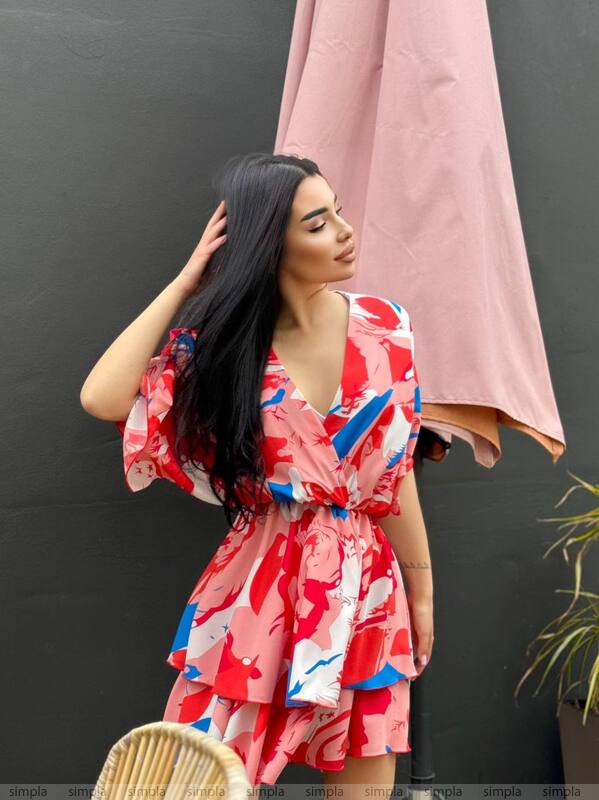 Woman in a colorful dress standing against a dark wall with a pink towel.