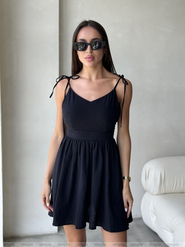 Woman wearing a black dress with thin straps in a minimal indoor setting