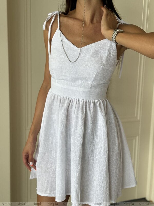 White dress with thin straps being adjusted against a neutral background