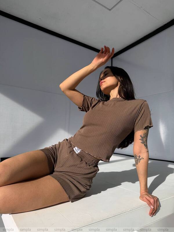 Woman in brown outfit posing against a white wall