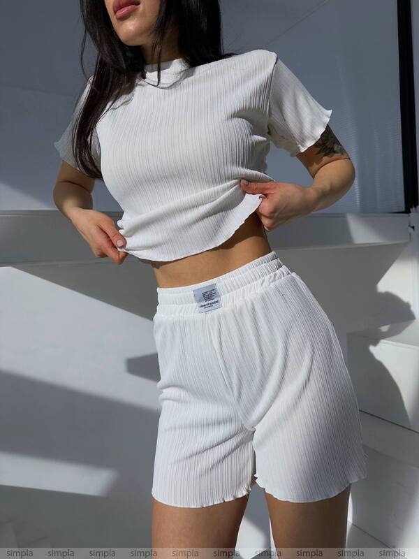 Person wearing a white ribbed crop top and shorts with a blurred background