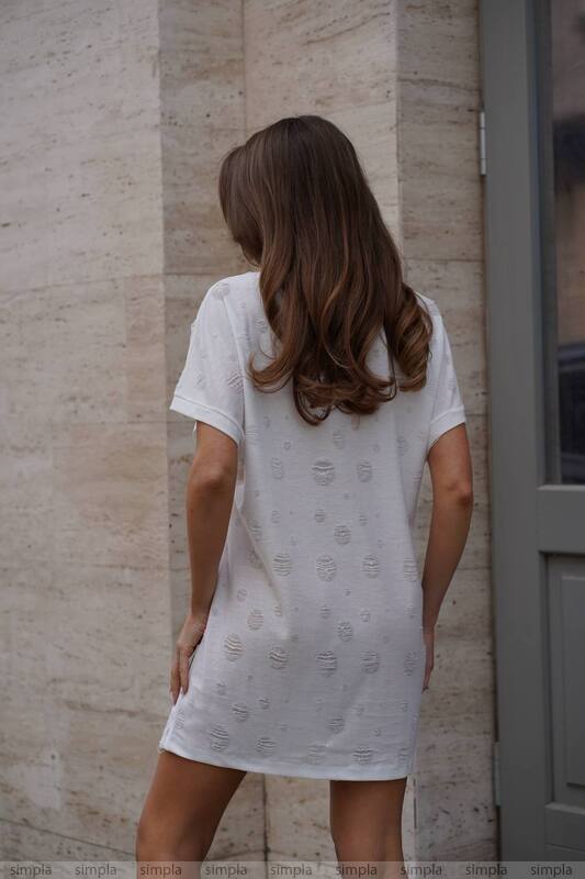 Woman wearing a white dress with a subtle pattern against a beige wall.