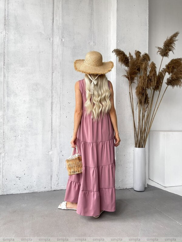 Woman in a long pink dress and straw hat standing in front of a white wall with pampas grass.