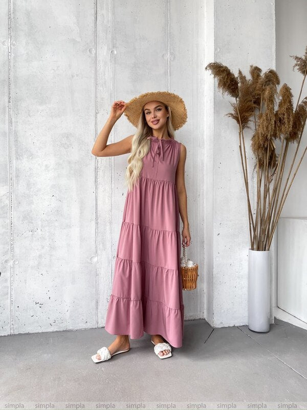Woman in a pink dress and straw hat standing against a white wall with decorative elements.