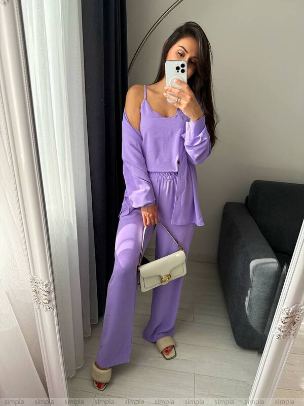 Woman in a purple outfit taking a mirror selfie in a room.