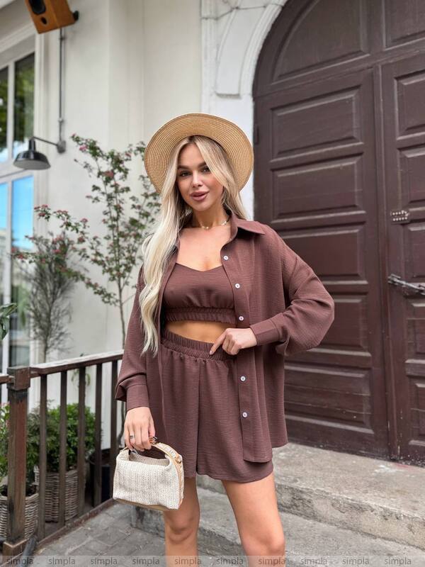Woman in a brown outfit with a hat standing in front of a building entrance.