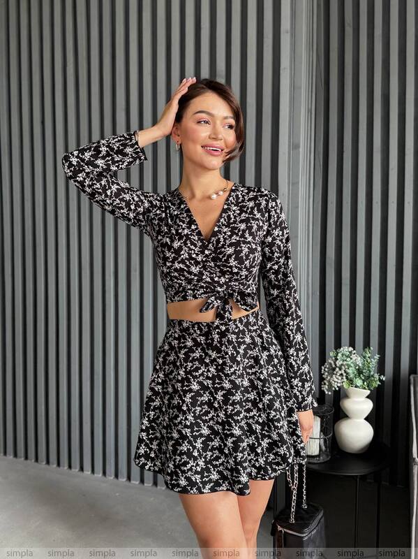 Woman wearing a black and white patterned dress against a striped wall.