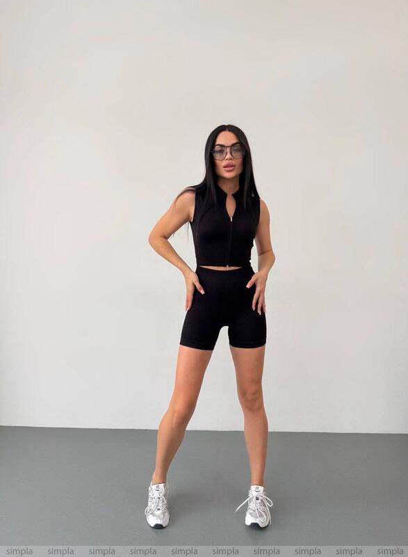 Person wearing a black outfit with white sneakers on a plain background
