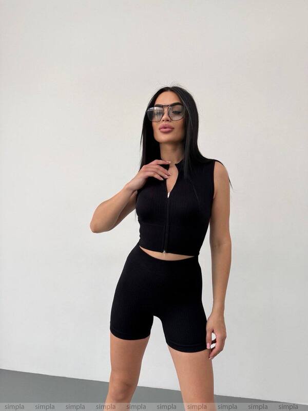 Woman wearing a black sleeveless top and high-waisted shorts against a white background