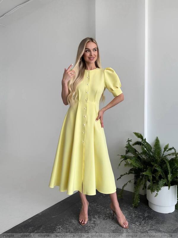 Woman wearing a yellow dress standing in a room with a plant.