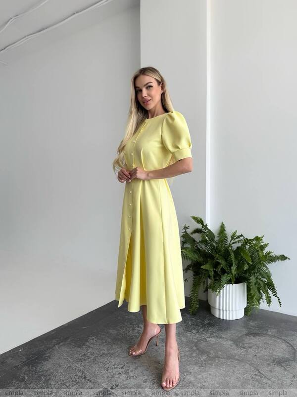 Woman in a yellow dress standing in a minimalistic room with a plant.