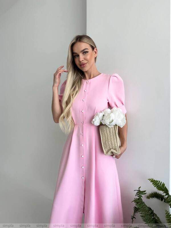 Woman wearing a pink dress holding flowers against a plain background