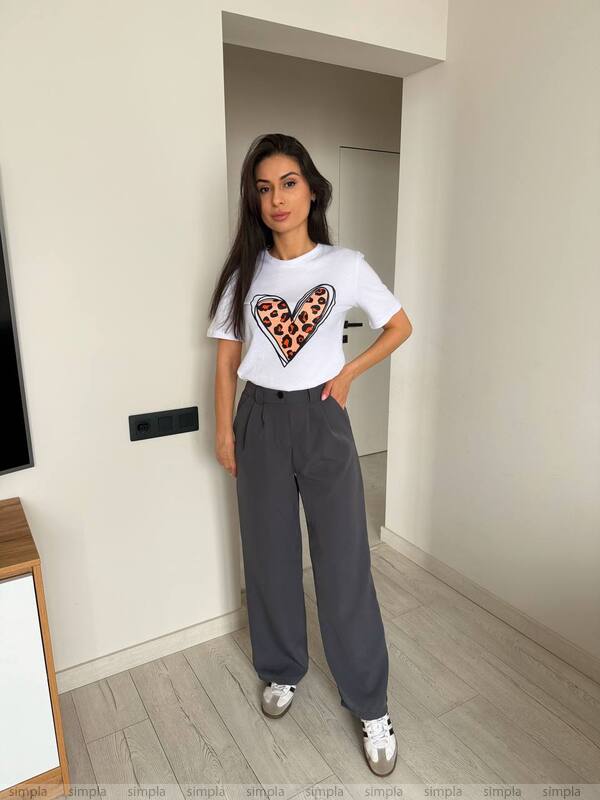 Woman wearing a white t-shirt with a heart design and gray pants in a room.