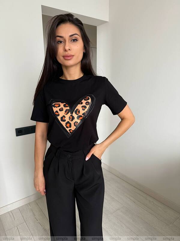 Woman wearing a black t-shirt with a leopard print heart design in a minimal indoor setting.