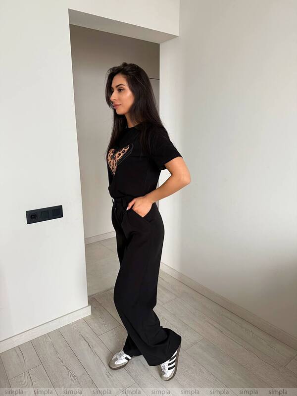 Woman wearing a black outfit with a graphic design in a minimalistic room.